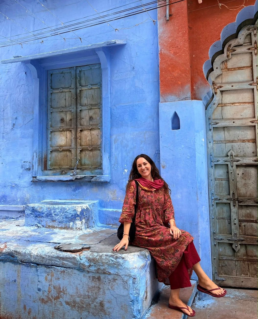 Natasha Barnett, your House of Raj host, seated beside blue walls in India